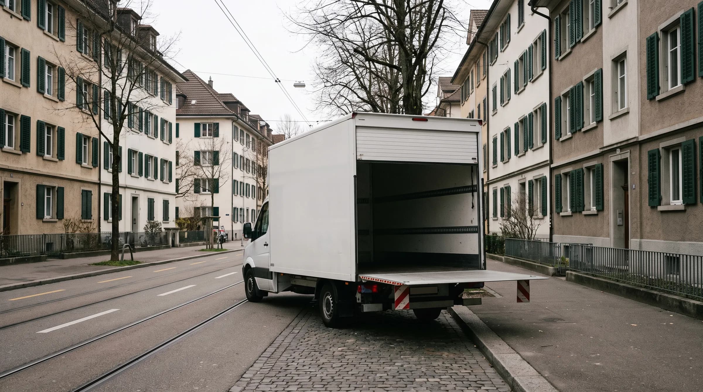 Möbelwagen mit geöffneter Ladebordwand am Strassenrand einer Wohnstrasse mit Tramgleisen.